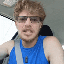 a man wearing glasses and a blue tank top has a necklace with a pendant that says jesus on it