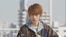 a young man wearing a jacket with a geometric pattern and a necklace with the letter l on it