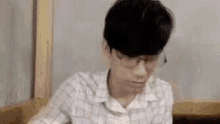 a young man wearing glasses and a plaid shirt is sitting at a table in a restaurant .