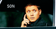 a man is talking on a cell phone in a car and the word son is on the window