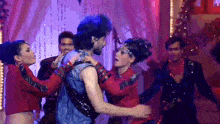 a group of people are dancing on a stage with purple lights in the background