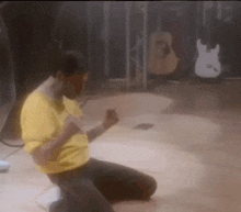 a man in a yellow shirt is kneeling on the floor in a dark room .
