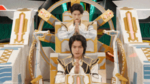 two men are sitting on a throne with their hands folded in front of them