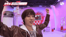 a man in a brown leather jacket holds his fist in the air in front of a sign that says mnet