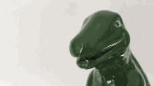 a green ceramic dinosaur is sitting on a white surface .