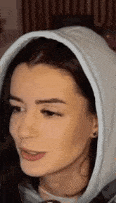 a close up of a woman wearing a white hoodie and earrings .