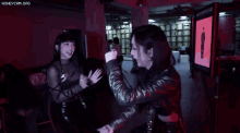 two women are dancing in a dark room with the words honeycam.org written on the bottom