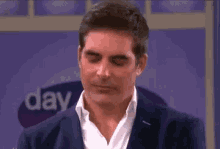 a man in a suit and white shirt is standing in front of a purple sign that says day .