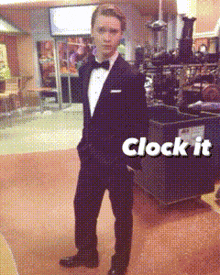 a man in a tuxedo is standing in front of a sign that says clock it on it