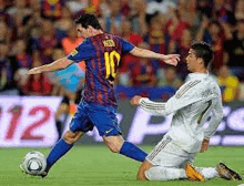 a soccer player is kicking a soccer ball while another player is kneeling on the ground .