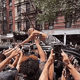 a crowd of people are holding up their phones to take a picture of a woman standing on top of a car .
