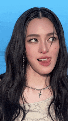 a woman wearing a necklace with a cross on it sticks her tongue out