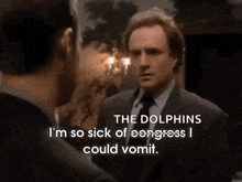 a man in a suit and tie is talking to another man and says the dolphins