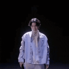 a young man in a white jacket is standing in a dark room and looking at the camera .
