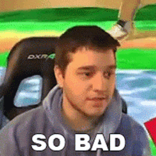 a man in a hoodie is sitting in a chair with the words `` so bad '' written on his face .