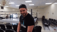 a man wearing a black adidas shirt is standing in a room with chairs