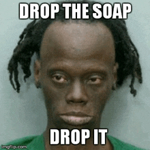 a man with dreadlocks is wearing a green shirt and has the words `` drop the soap drop it '' written on his face .