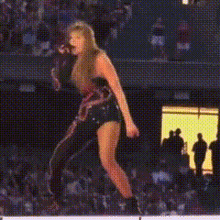 a woman in a black dress is jumping in the air while singing into a microphone on a stage .