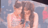 two women are standing next to each other on a stage looking at their phones .