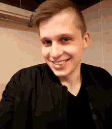 a man in a black jacket and black shirt smiles for the camera