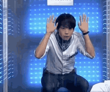 a man is kneeling down in front of a glass wall with his hands up in the air .