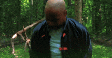 a man in a blue jacket with red sleeves is standing in the woods