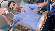 a man in a blue striped shirt is cooking spaghetti in a frying pan