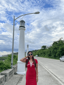 a woman in a red dress stands next to a white lighthouse