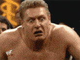 a shirtless wrestler is making a funny face in front of a crowd .