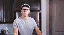 a man wearing glasses and a baseball cap is standing in front of a refrigerator