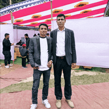 two men standing next to each other in front of a pink and white canopy