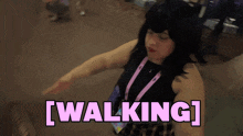 a woman wearing a black top and a purple lanyard is walking