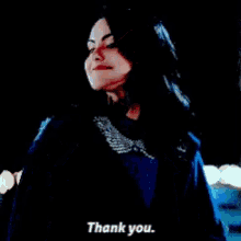 a woman in a blue jacket is standing in the dark and saying `` thank you '' .