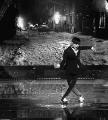 a black and white photo of a man dancing in a snowy street