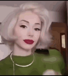 a woman with blonde hair and red lipstick is wearing a green sweater and necklace .
