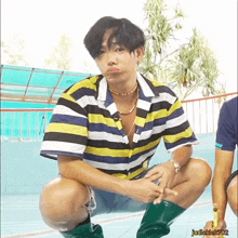 a man wearing a striped shirt and green boots is squatting in front of a pool
