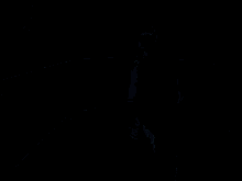 a man with a beard is standing in a dark room while another man sits on a bench