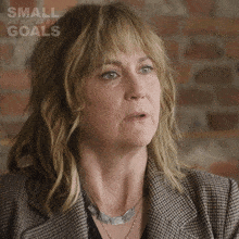 a woman wearing a plaid jacket and a silver necklace with the words small achievable goals on the bottom