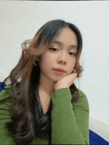 a young woman in a green shirt holds her hand to her chin