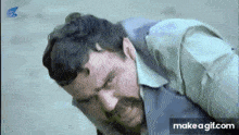 a man with a beard is laying on the ground with his head on his knees .