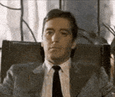 a man in a suit and tie is sitting in a chair and making a funny face .