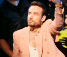 a man with a beard is wearing a pink jacket and a white tank top .