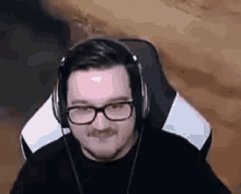 a man wearing glasses and headphones is sitting in a gaming chair .