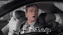 a man in a suit and tie is sitting in the driver 's seat of a car with his mouth open .