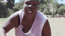 a man in a white tank top is standing in a field with his tongue out .