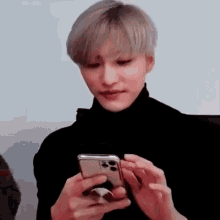 a man in a black turtleneck is holding a cell phone in his hands .