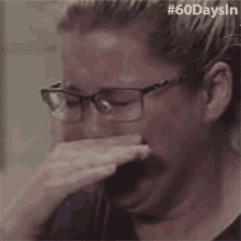 a woman wearing glasses is crying while covering her mouth with her hand .