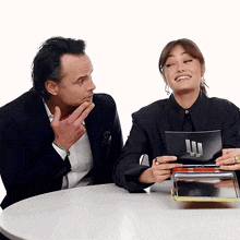 a man and a woman are sitting at a table and the woman is holding a piece of paper that says " i love you "
