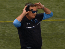 a man wearing sunglasses and a under armour shirt stands on a field
