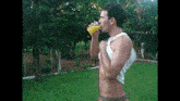 a shirtless man drinking orange juice in a park